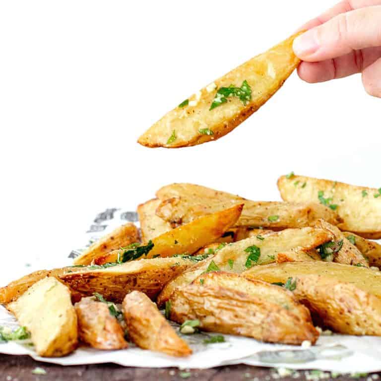 Single parsley sprinkled baked potato wedge being lifted from a pile.