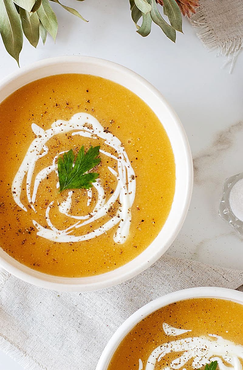 White bowl with pumpkin soup, cream drizzle, on a marble background