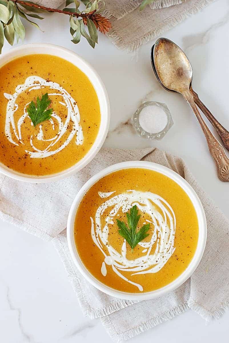 Two white bowls with pumpkin soup, spoons, salt, white background