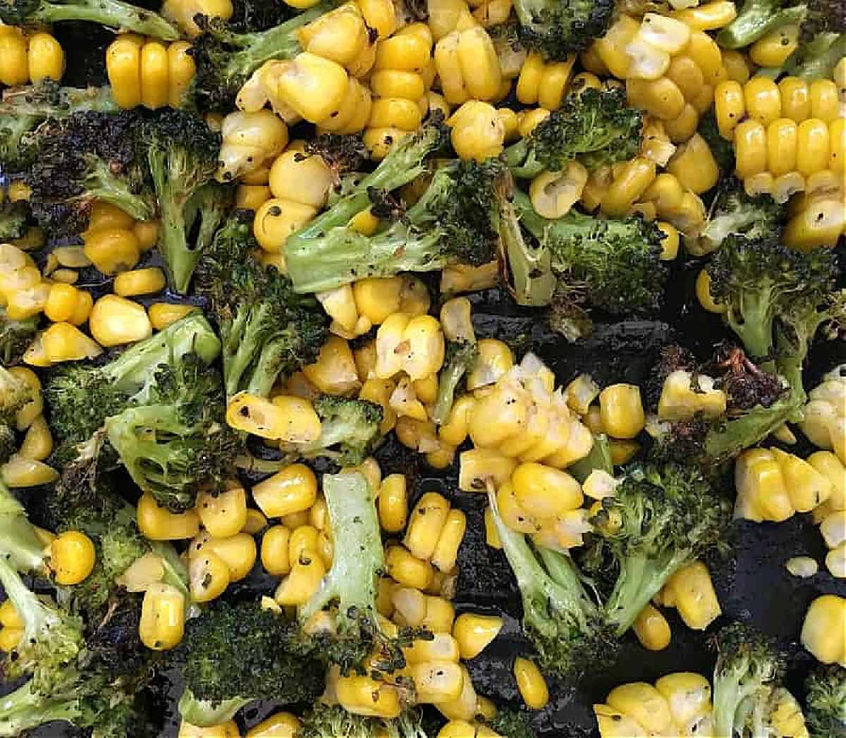 Roasted corn and broccoli pieces on a black tray.