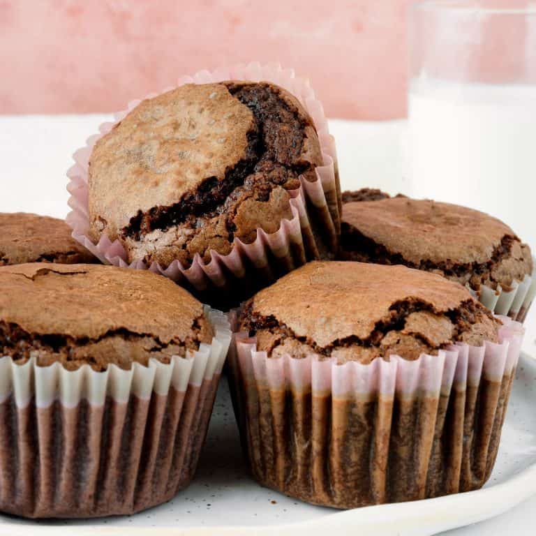 Small pile of brownie muffins in paper liner with a pink background.