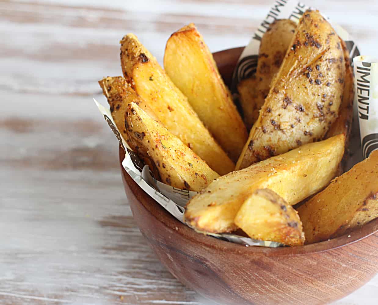 Small wooden bowl with skin-on potato wedges, a whitish surface