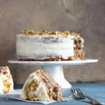Slices of frosted layer cake on blue background, whole cake in white cake stand