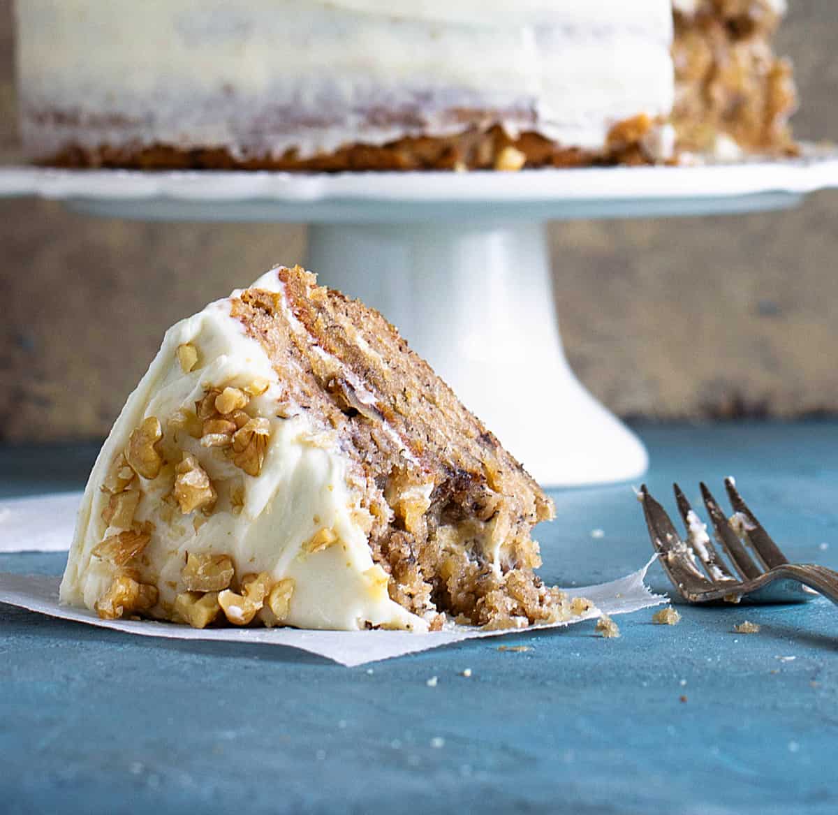 Slice of frosted layer cake on blue background, fork