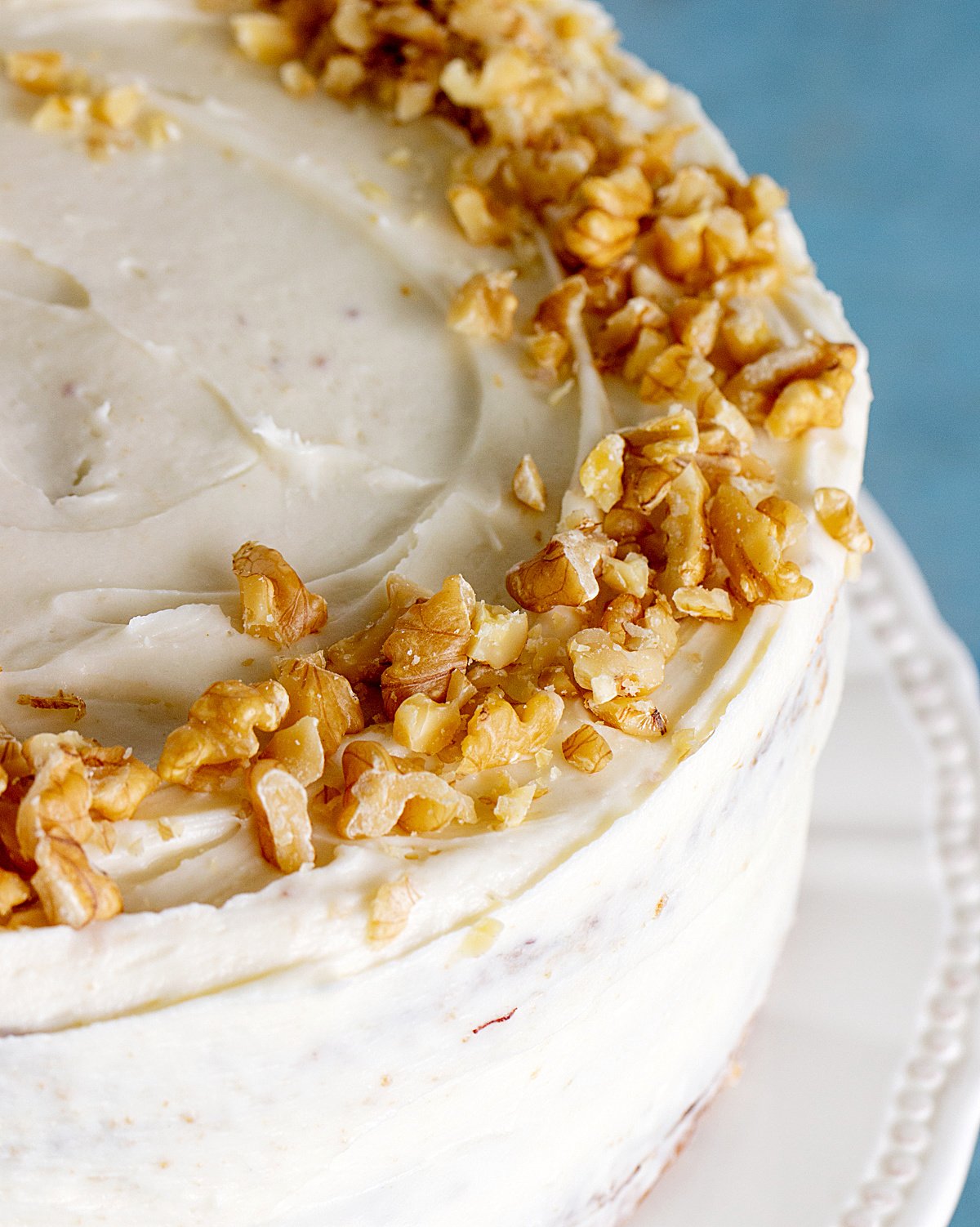 Partial top view of whole frosted cake on a white cake stand with walnuts on top.