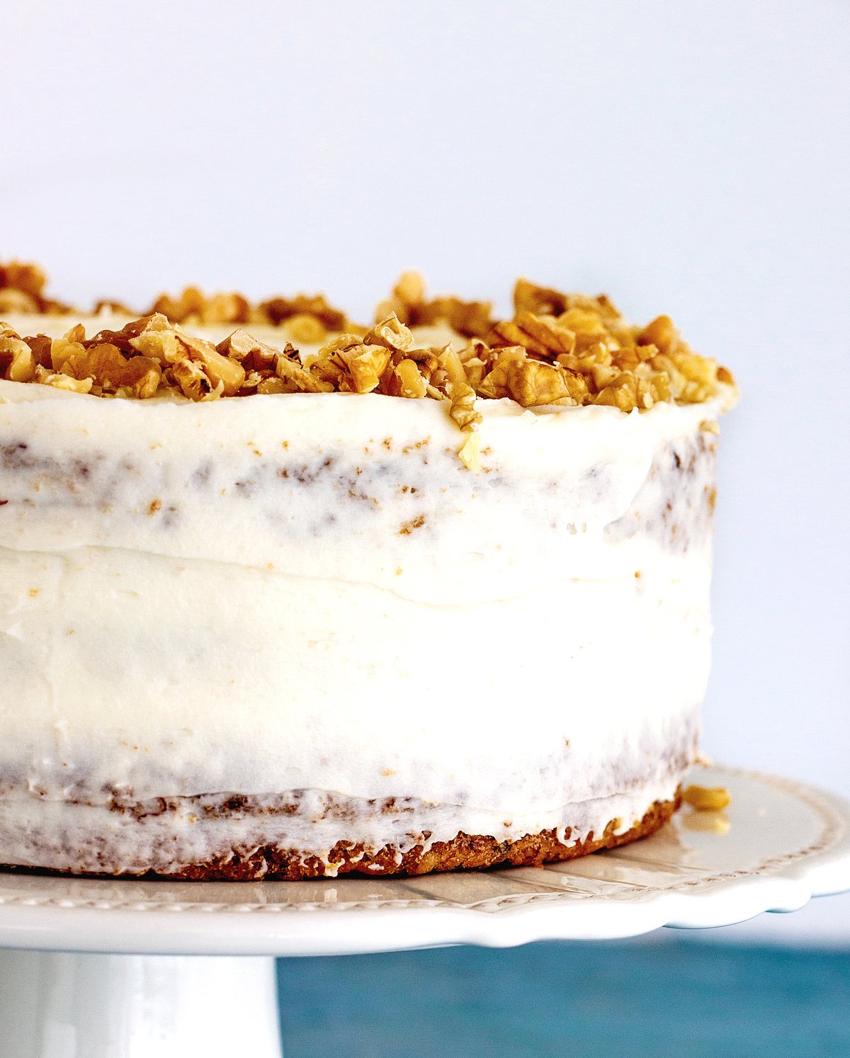 Partial view of whole frosted cake on a white cake stand with walnuts on top