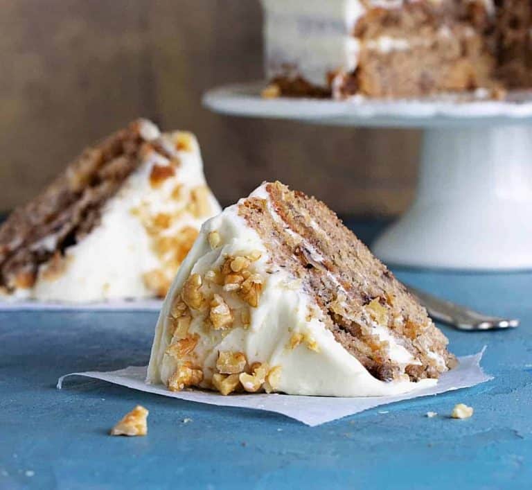 Slices of frosted layer cake on blue background, whole cake in white cake stand