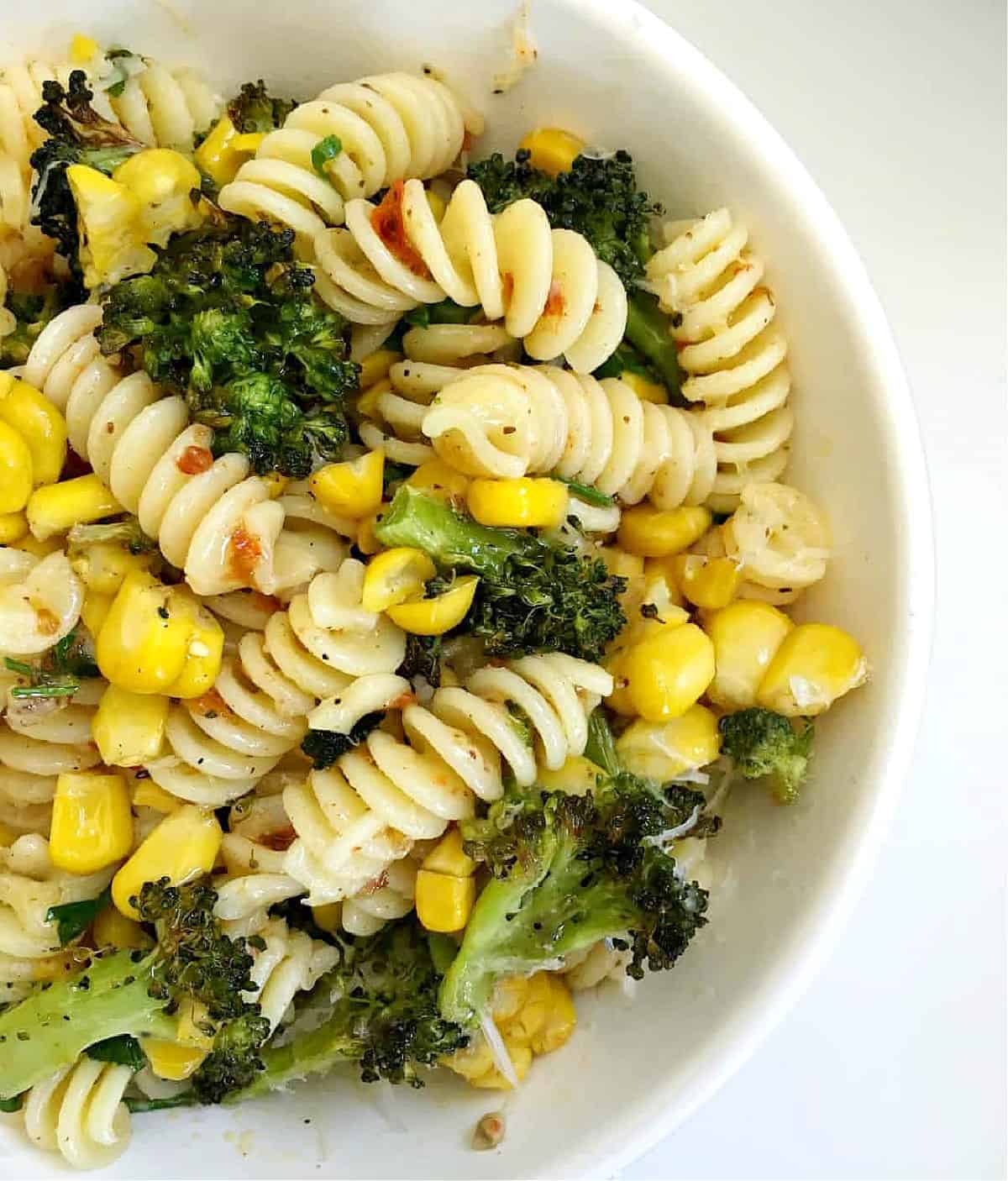 Close up of white pasta bowl with corn and broccoli.