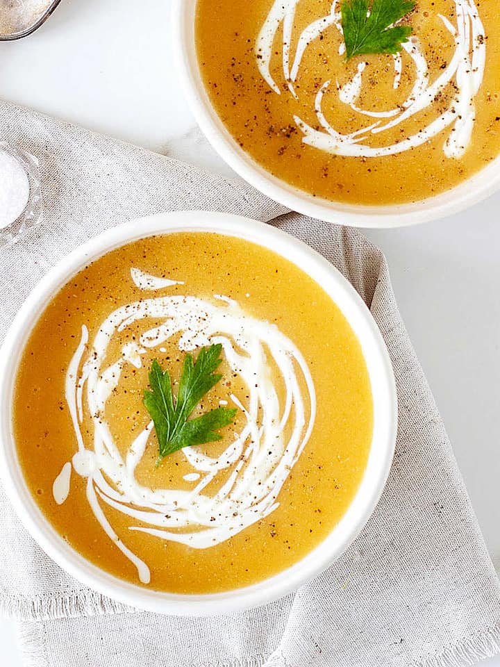 Pumpkin soup with cream drizzle on white bowls. Beige cloth on white surface.