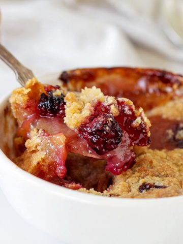 Spooning some apple blackberry crumble from a white bowl. White background.