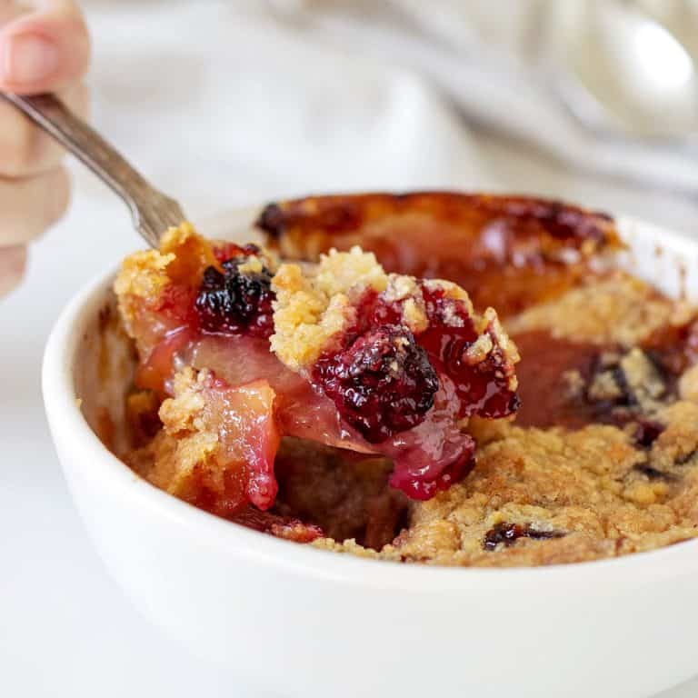 Spooning some apple blackberry crumble from a white bowl. White background.