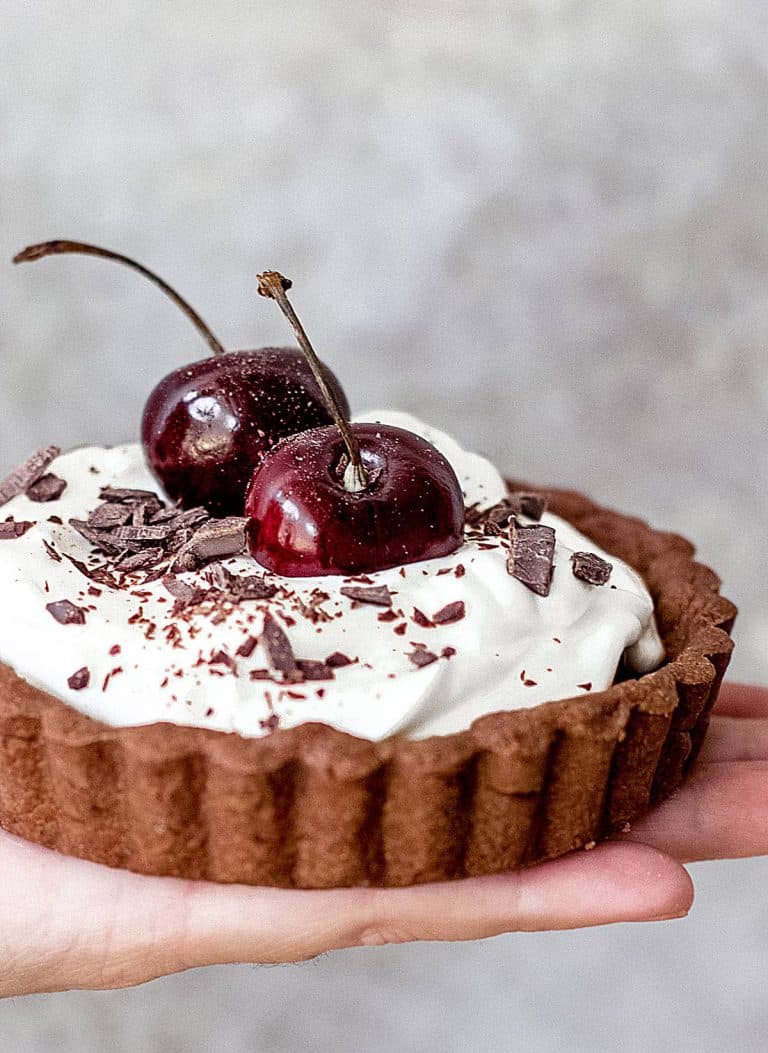 Hand holding small chocolate cream tart with whole cheeries on top