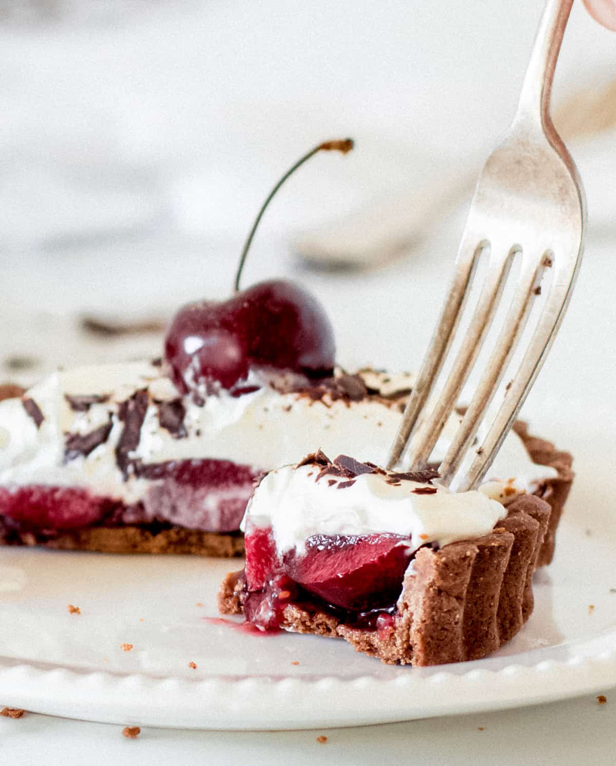 Close-up of a fork about to lift a piece of chocolate, cherry and cream tartlet; half tart beneath