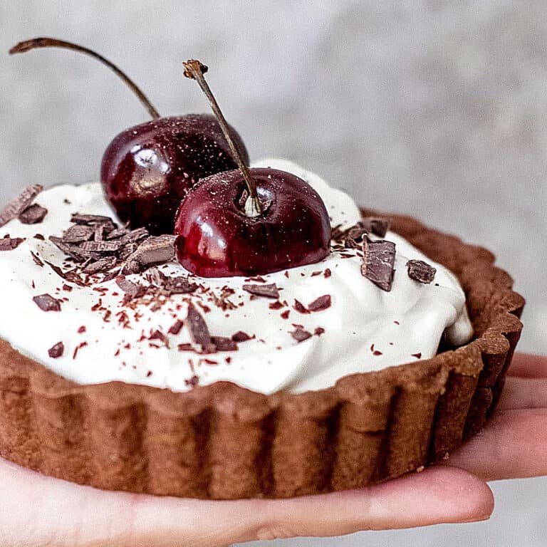 Close up of chocolate cream tart with whole cherries on top. Gray background.