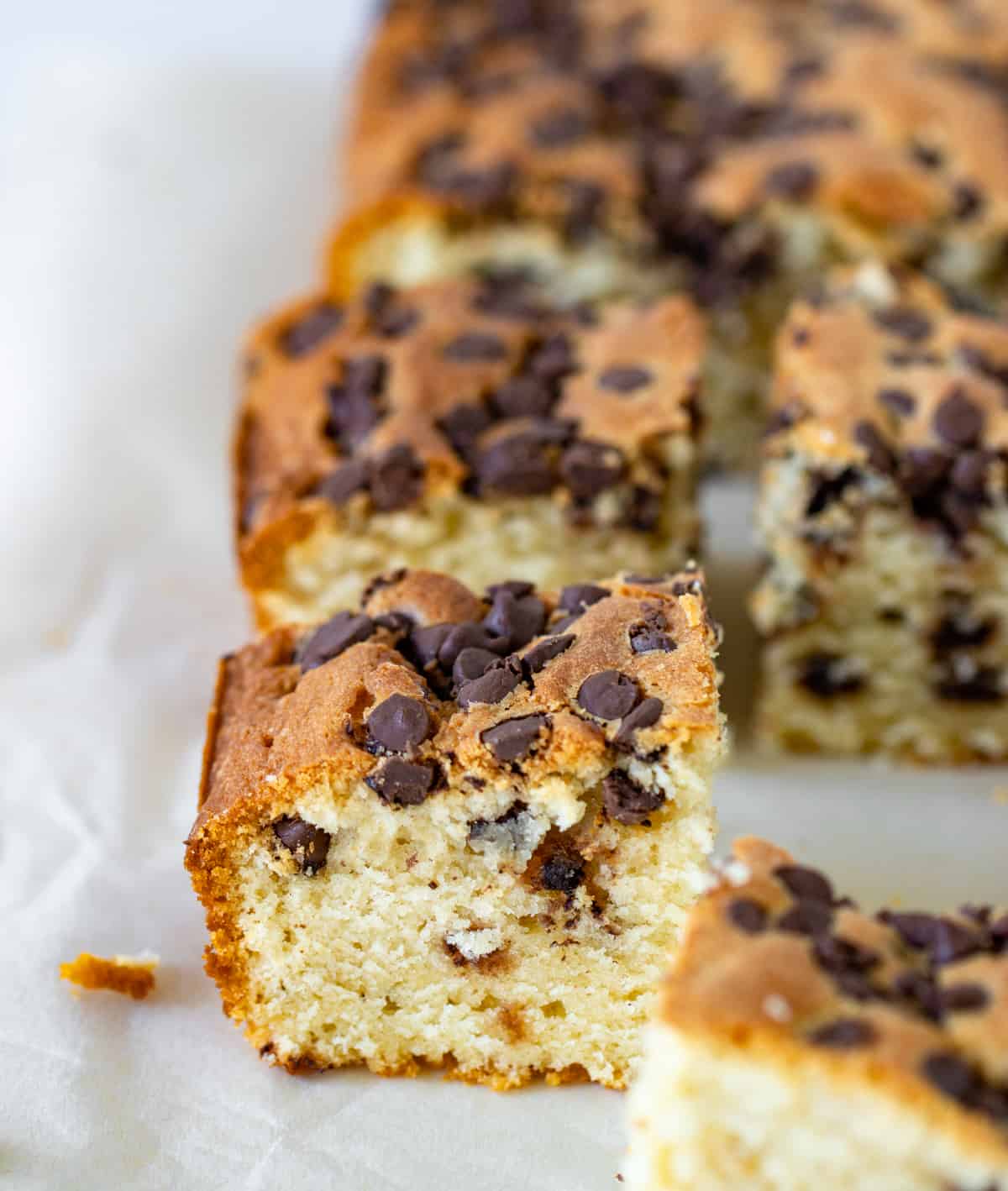 View from above of Squares of vanilla cake with chocolate chips on parchment paper.