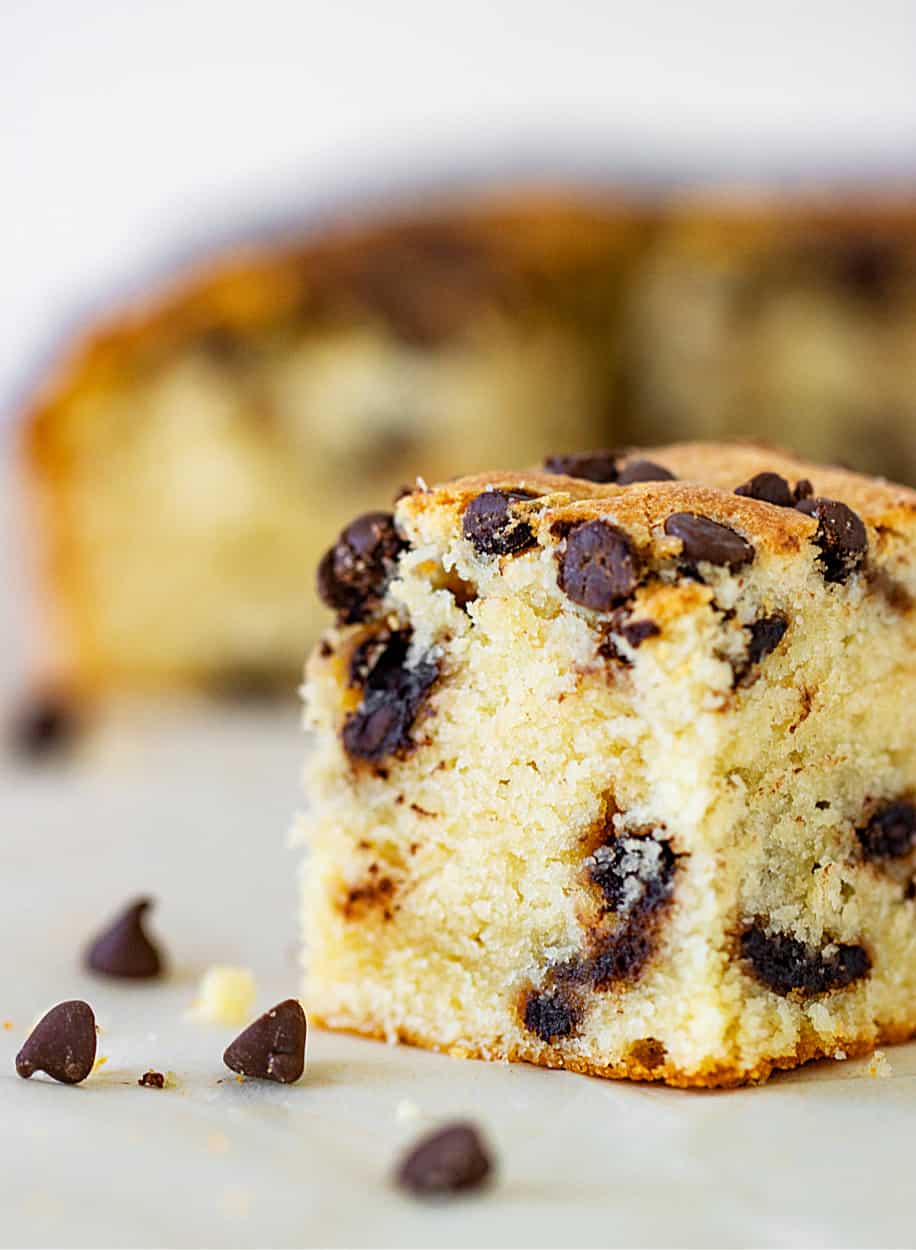Single square of vanilla cake with chocolate chips on white surface, loose chips around