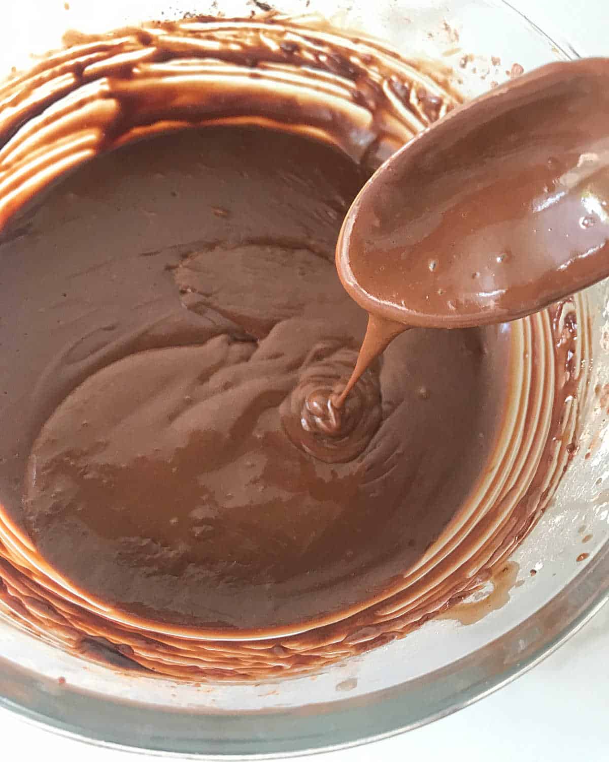 Wooden spoon lifting chocolate custard mixture from a glass bowl.