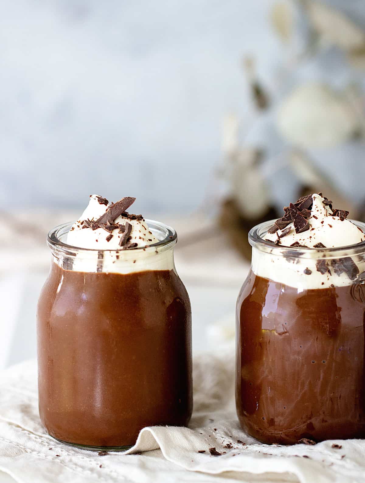 Two Glass jars with chocolate pudding and cream on white linen, grey background