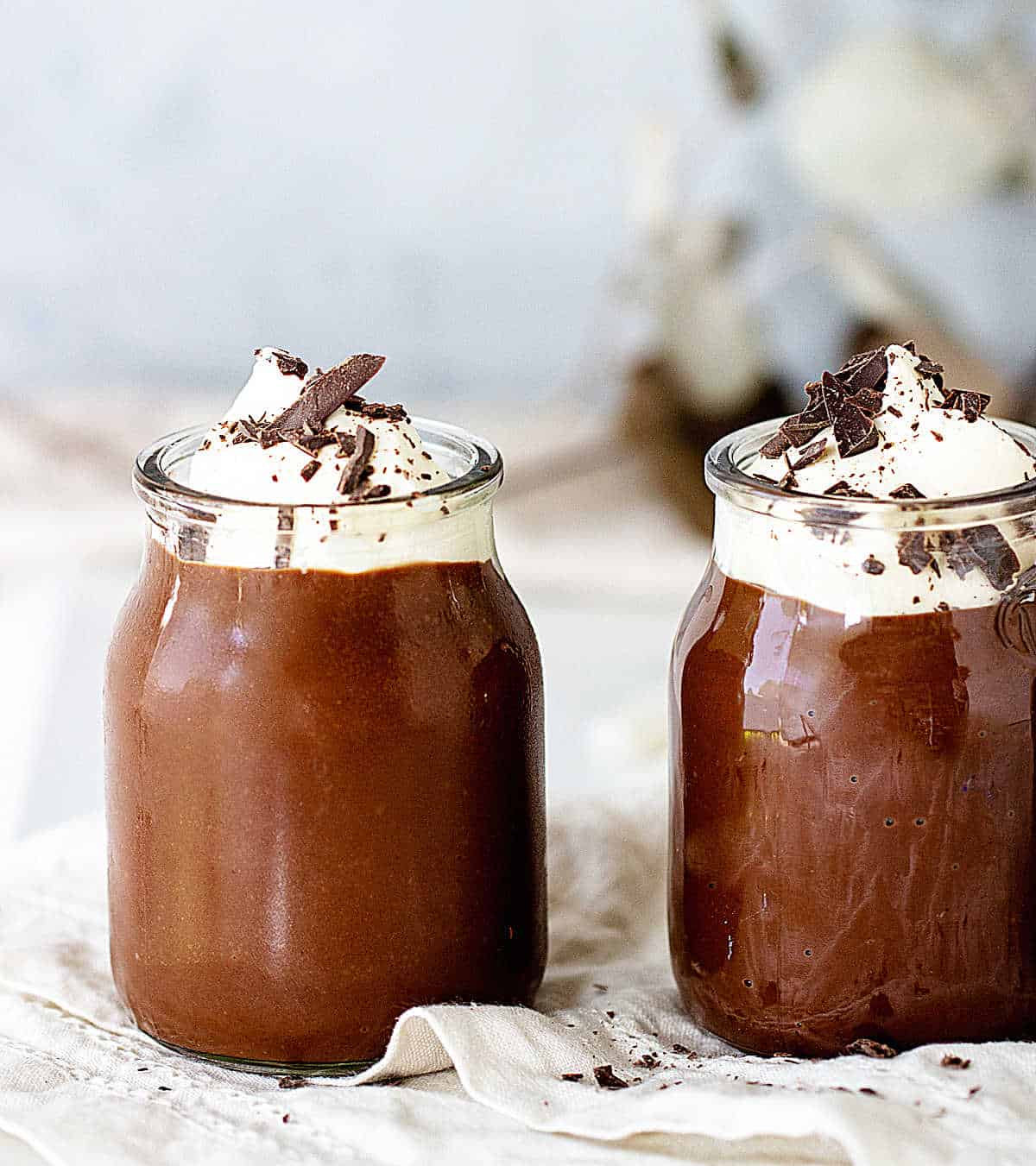 Frontal view of two jars with chocolate pudding, whipped cream and chocolate shavings on grey white background
