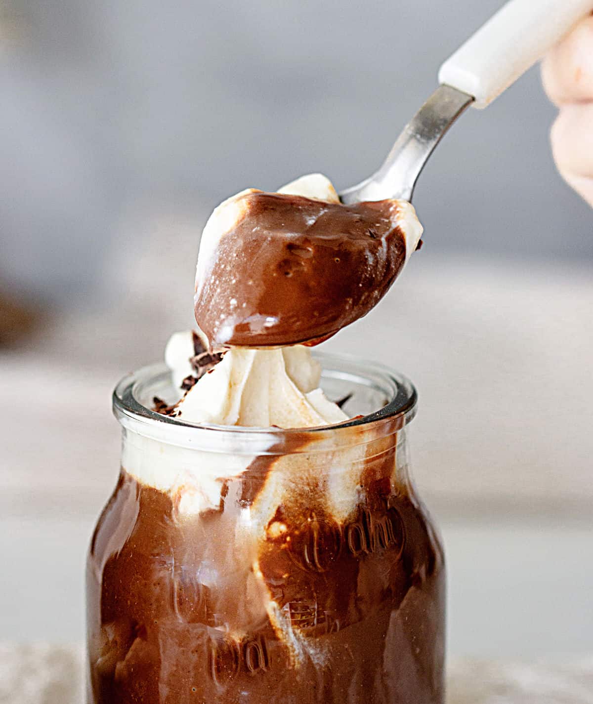 Hand spooning chocolate cream pudding from glass jar