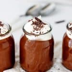 Glass jars with chocolate pudding and cream, grey background