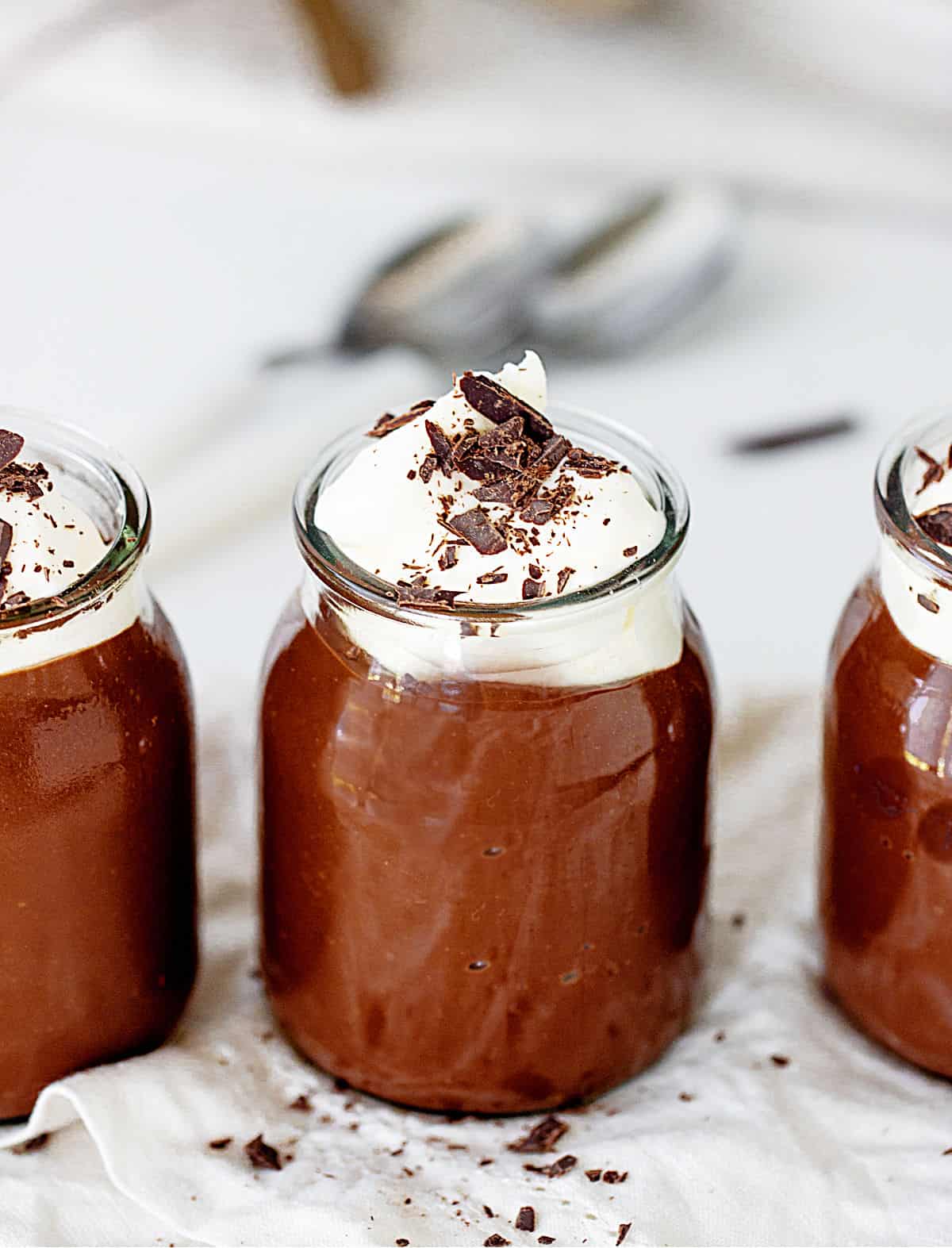 Glass jars with chocolate pudding and cream, grey background