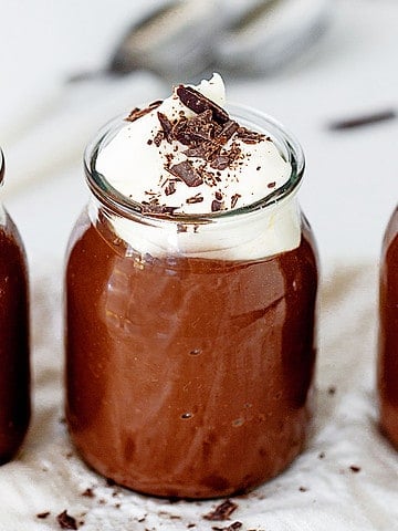 Close up chocolate pudding in jars with whipped cream and chocolate shavings. Grey background.