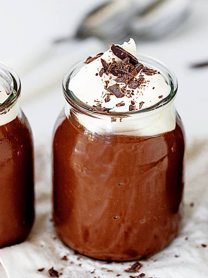 Close up chocolate pudding in jars with whipped cream and chocolate shavings. Grey background.