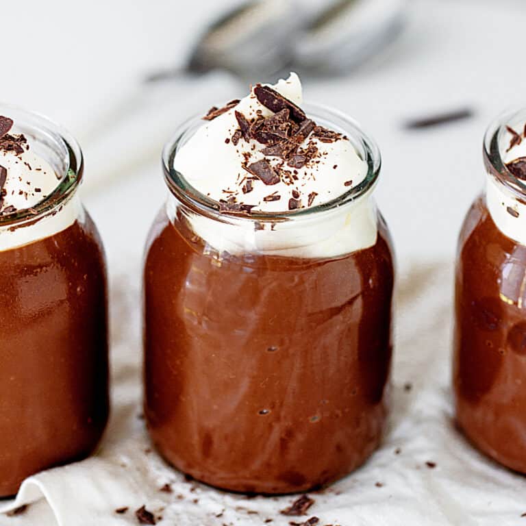Close up chocolate pudding in jars with whipped cream and chocolate shavings. Grey background.