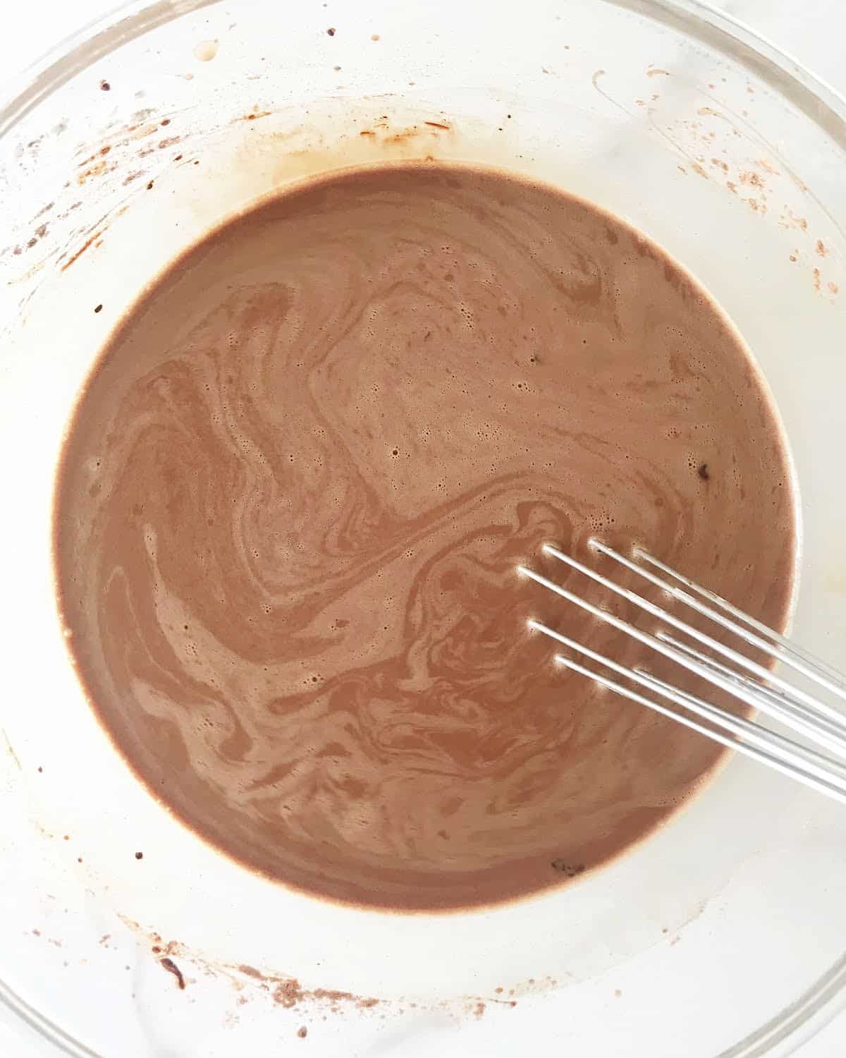 Chocolate milk in a glass bowl with a metal whisk inside.
