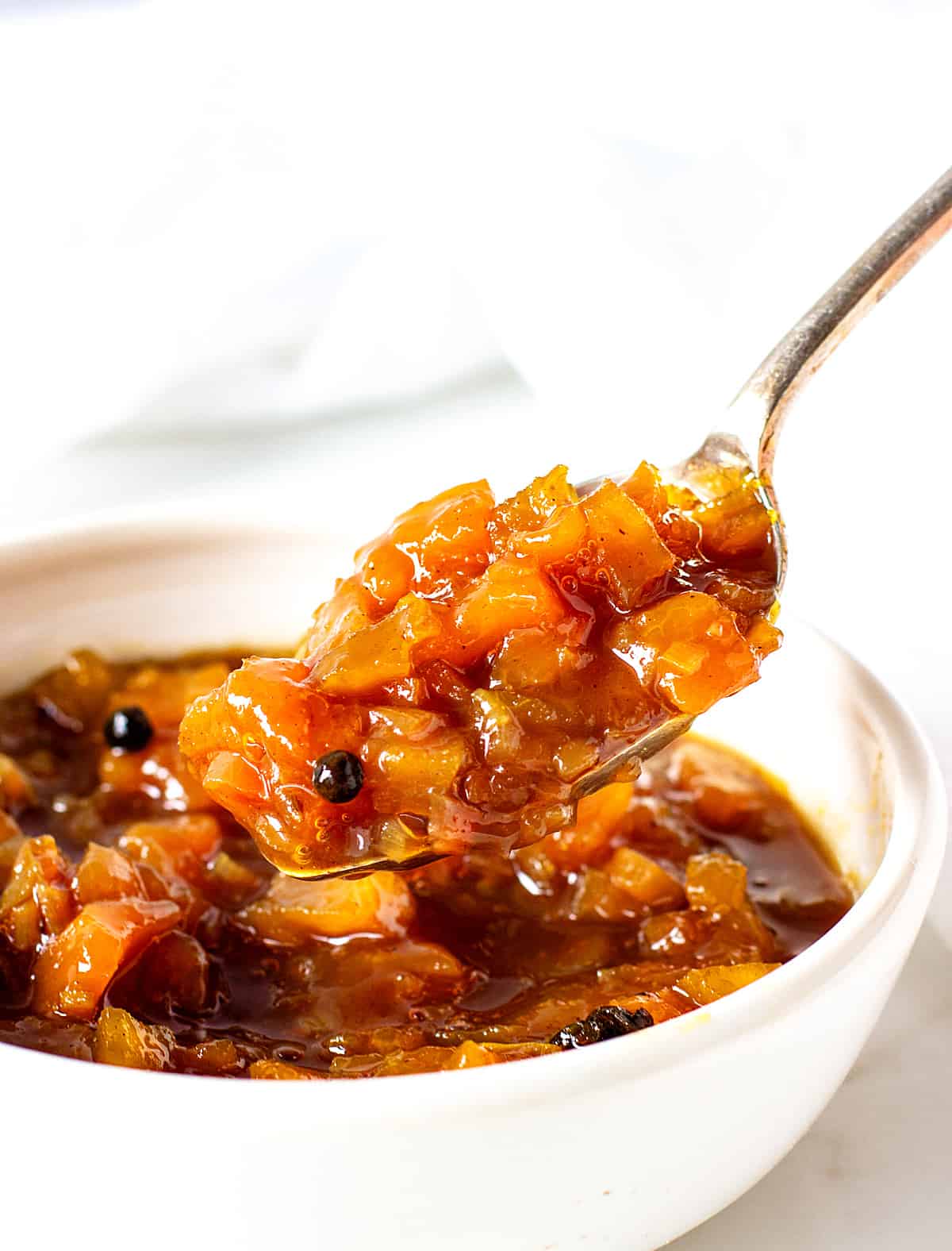 Lifting a spoon of peach chutney from white bowl.