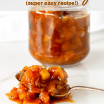 Silver spoon with peach chutney, glass jar in the background, white surface, image with text