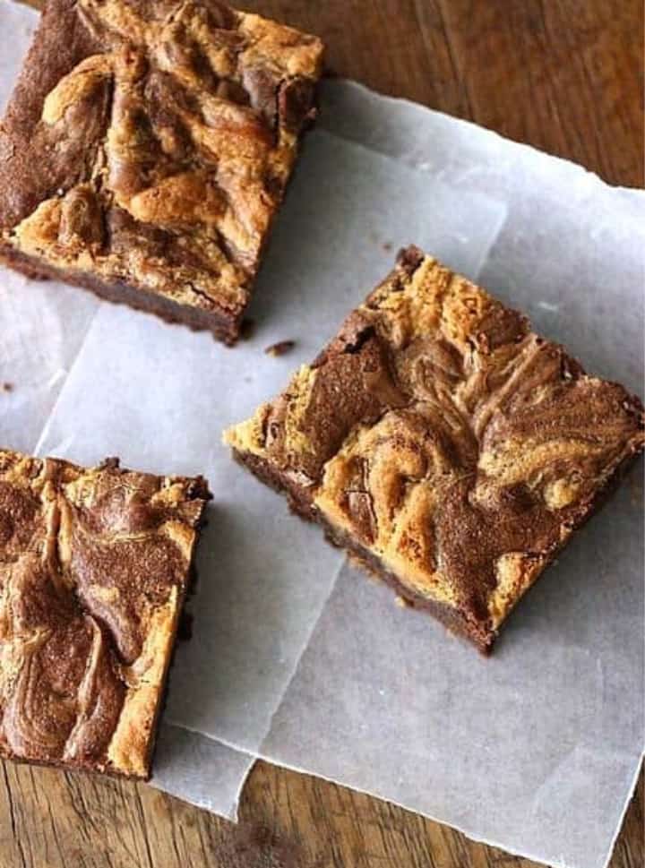 Squares of peanut butter brownies on parchment paper, wooden table.