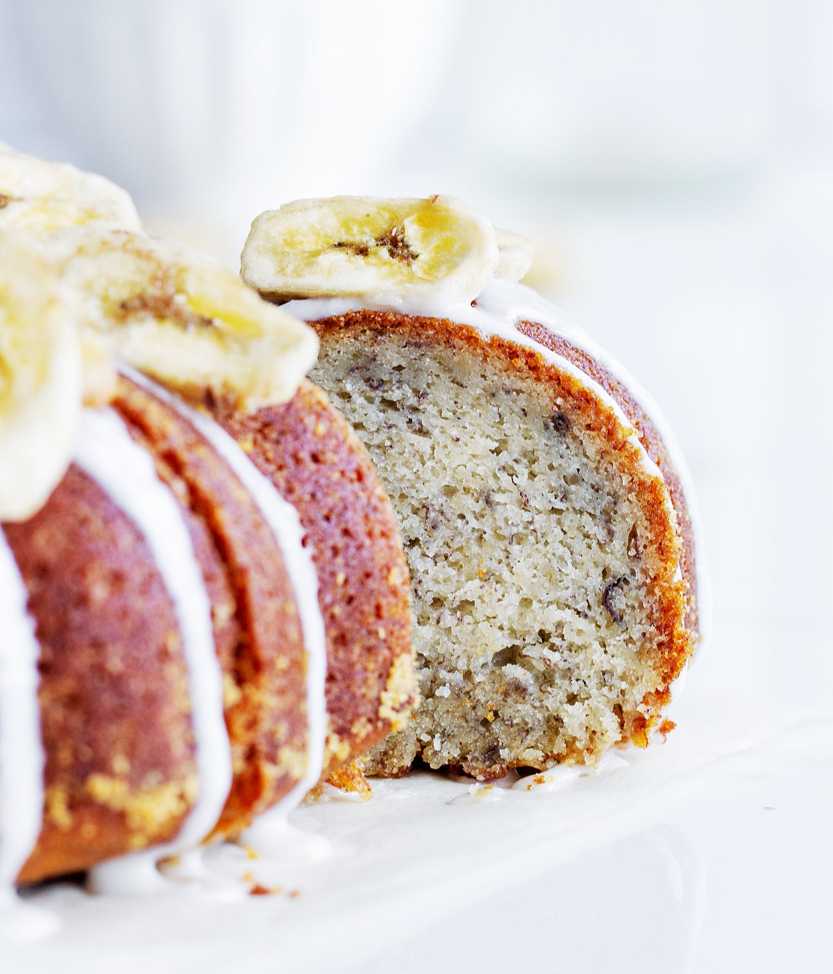 Slice of banana cake pulled out from whole bundt, white background