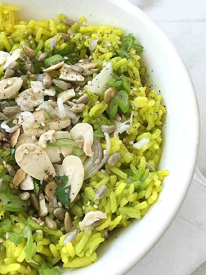 White bowl of green rice with almonds and seeds on white marble