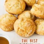 Pile of scones on a white surface, a honey bowl and brown text overlay.