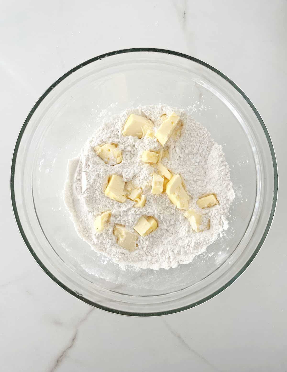 Top view of glass bowl on white marble with flour and butter pieces.