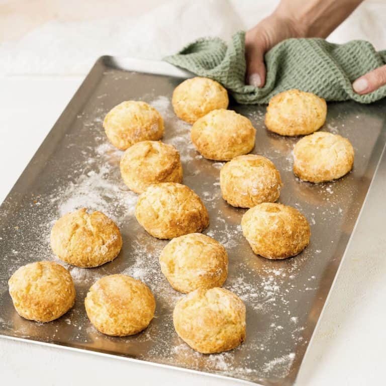 Hand holding metal tray with baked scones and a green cloth.