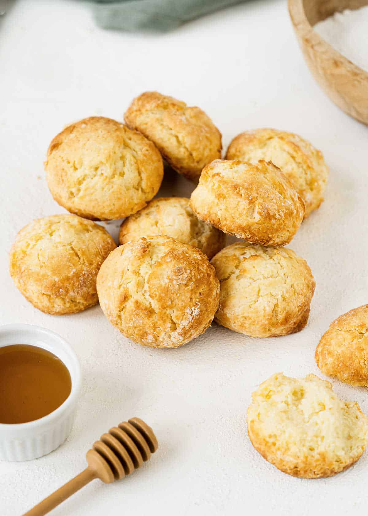 Scones piled up on a white surface with a honey pot.