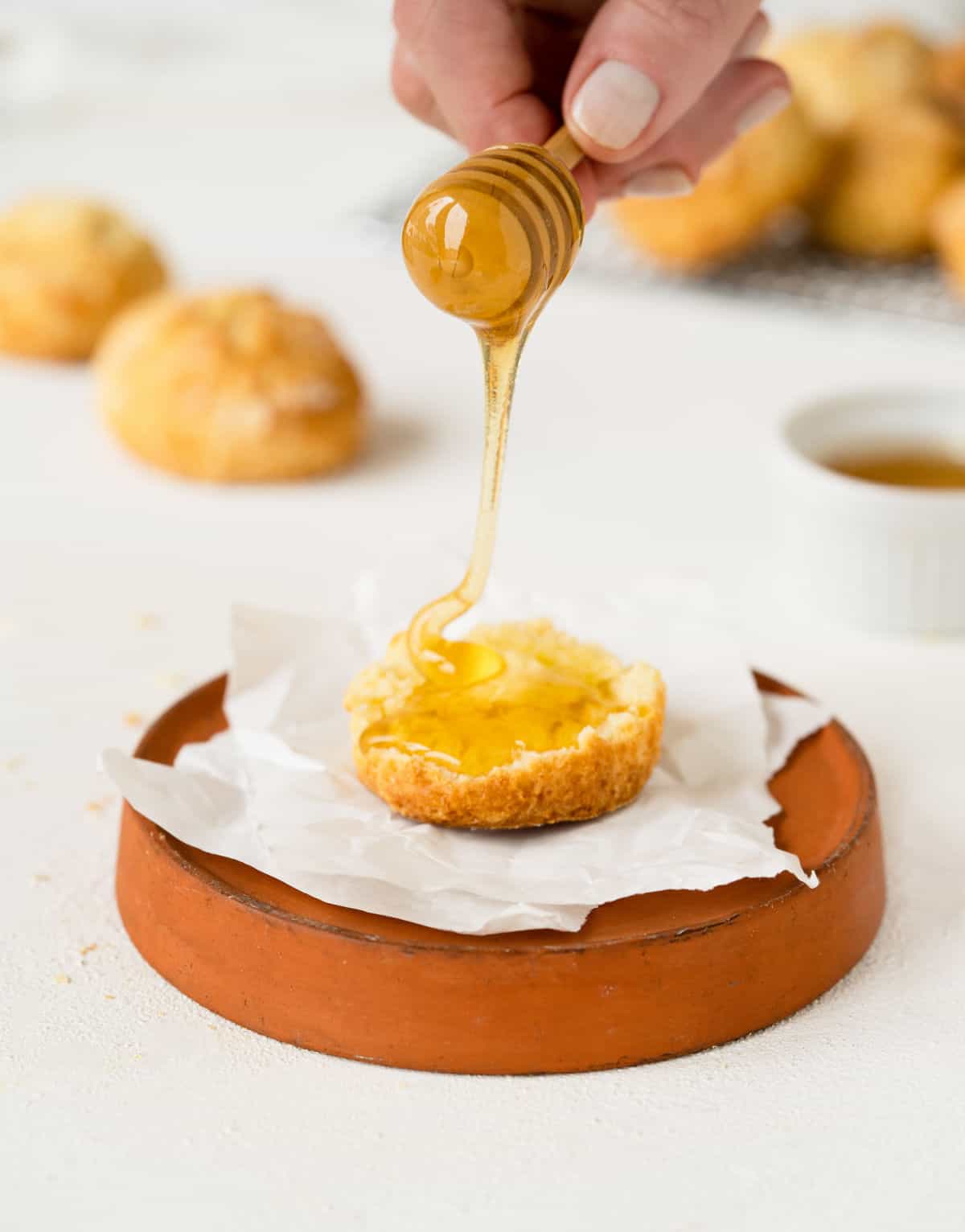 Honey being poured over half a scone on a orange plate. White surface.