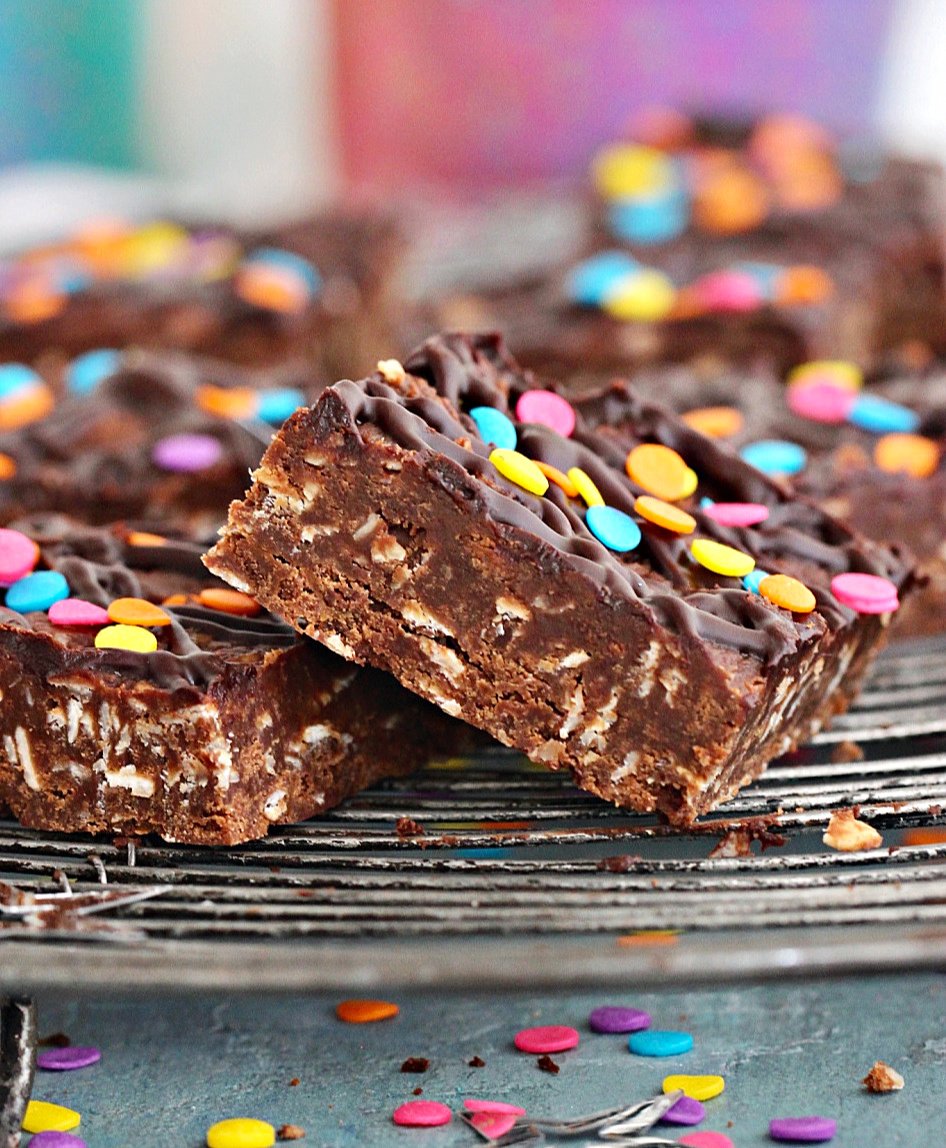 Close-up of Chocolate oat squares on a wire rack with confetti, bluish background.