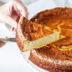 Lifting a slice of ricotta cheesecake from the whole cake on a white plate with a silver knife. White background.