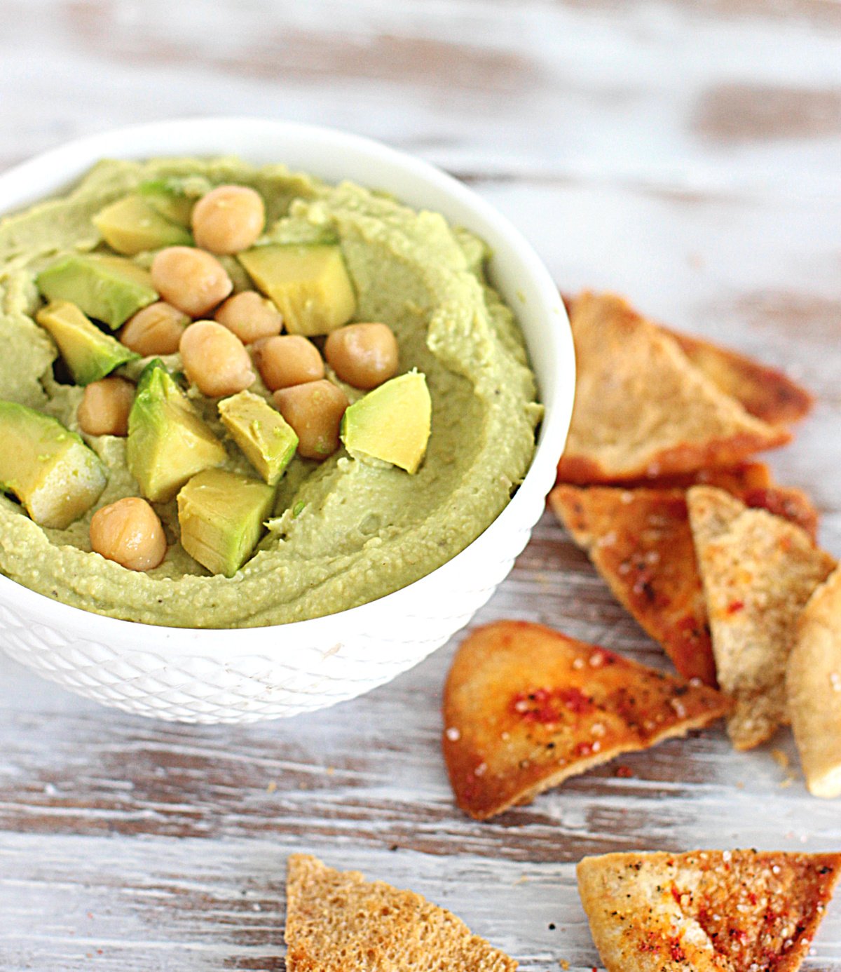 White bowl with green dip, chickpeas and pita chips; on white wooden table