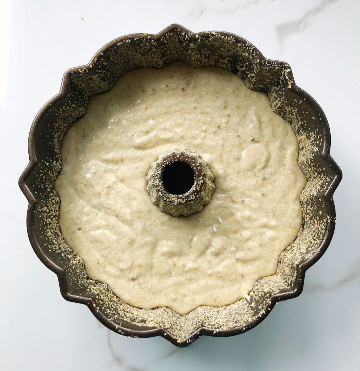 Bundt pan with cake batter on white marble.