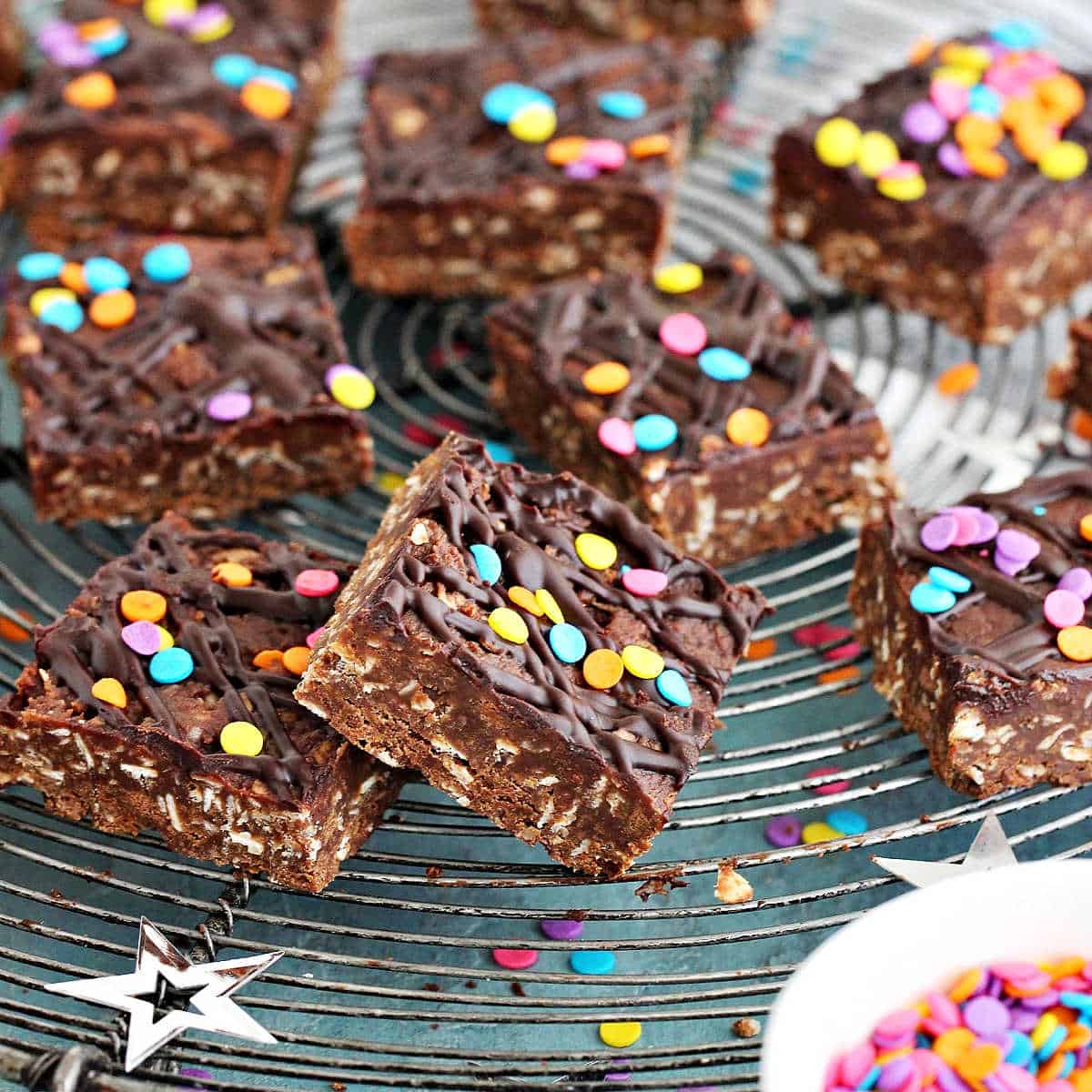 Pile of chocolate oat bars with confetti on a wire rack set on a blue surface. 