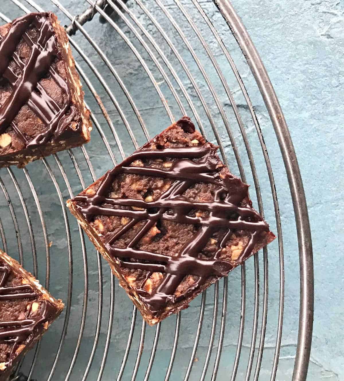 Wire rack on a blue surface with ganache topped chocolate oat bars.