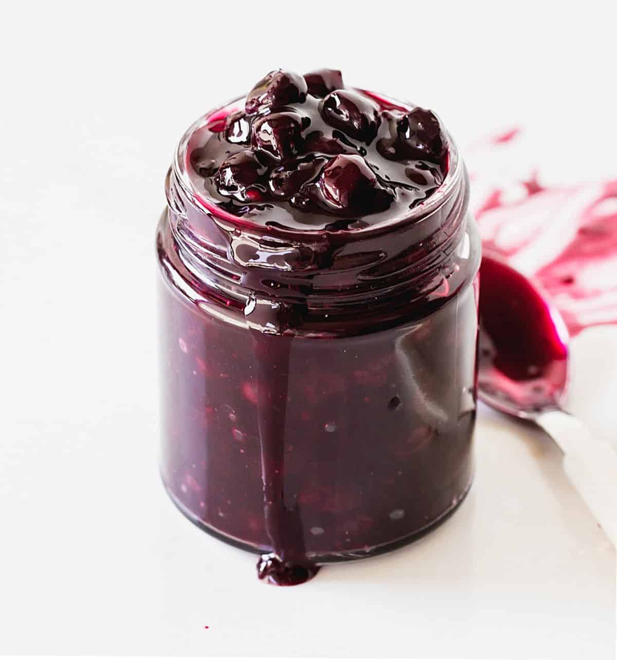 Glass jar with blueberry sauce, a spoon, white background
