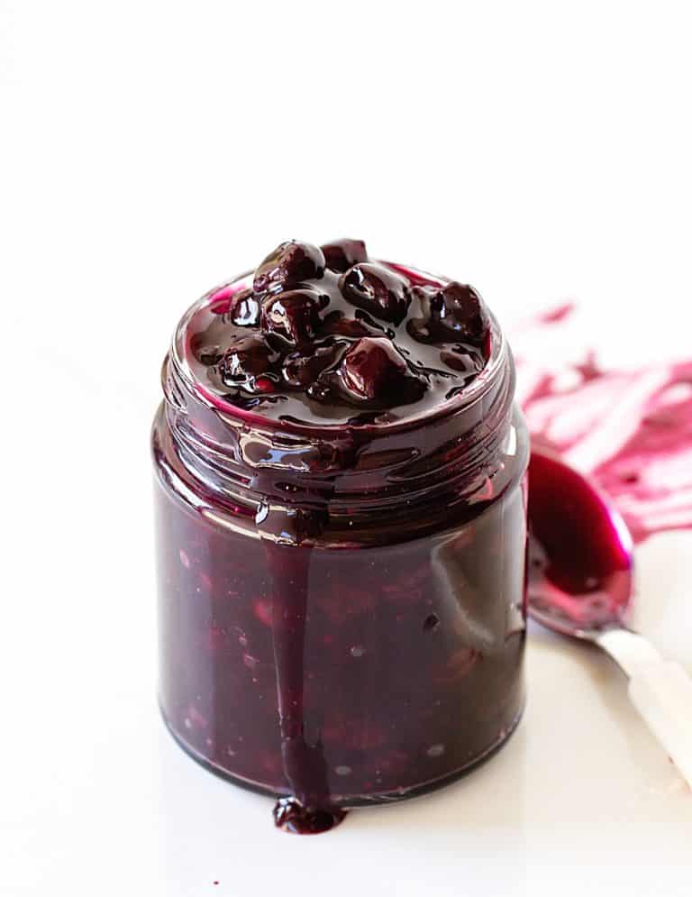 Glass jar with berry sauce on white surface, a spoon