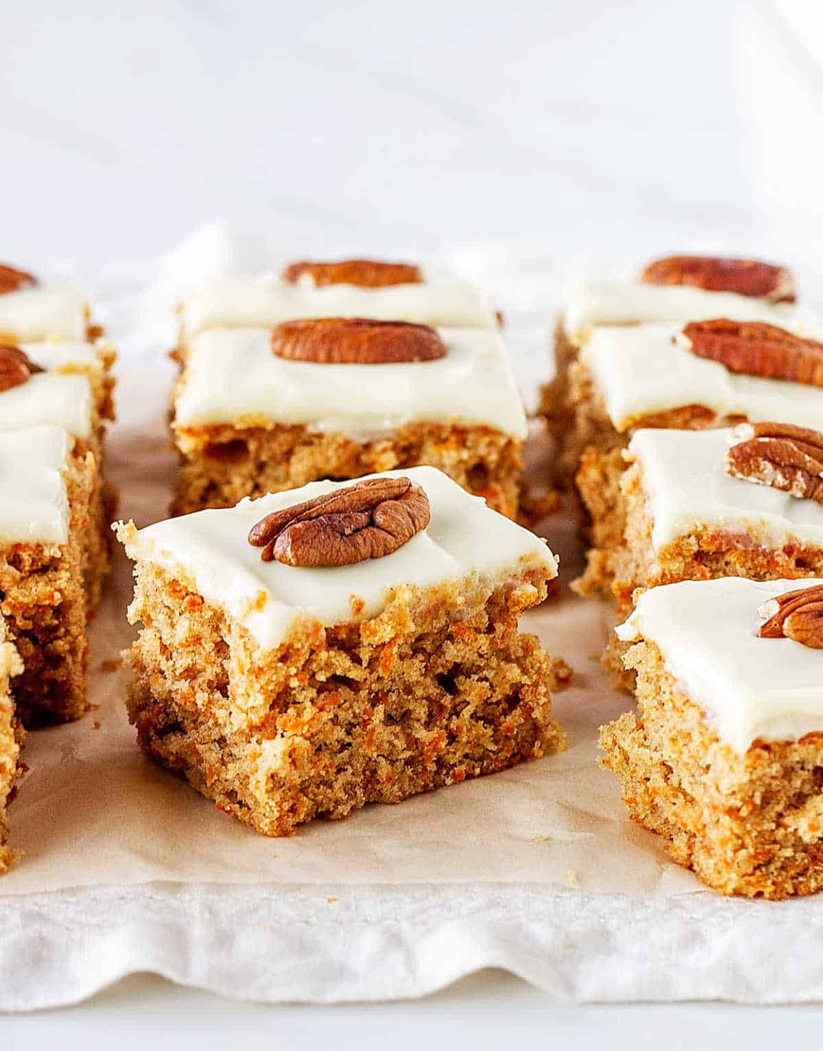 Squares of carrot cake with frosting and pecan, on white paper