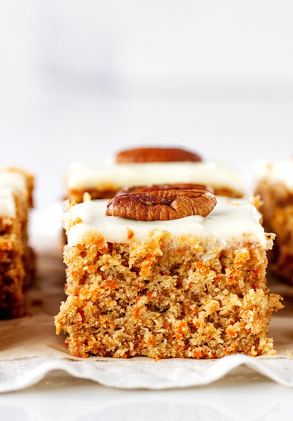 Close-up of square of frosted carrot cake with a pecan on top.